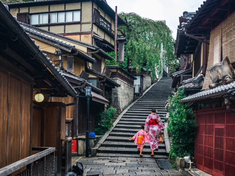 Verwinkelte Gassen in Kyoto. Ein Mutter geht gerade mit ihrem Kind eine lange Treppe hinauf.
